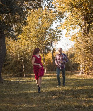 Genç aşık çift sonbahar parkında dinleniyor. Kaçıyorlar, eğleniyorlar ve gülüyorlar. Kırmızı elbiseli kız, kareli tişörtlü adam altın sonbahar arka planına karşı. 