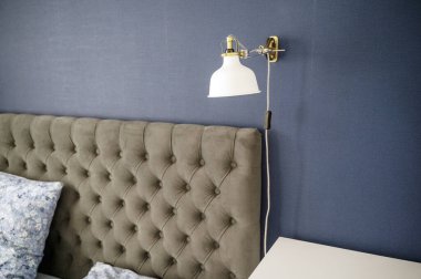 Yatak odasında yastıkları olan, modern döşenmiş yatak başlığı. Beyaz kolye lambası ve gri yatak başlığı, rahat minimalist yatak odası. Yüksek kalite fotoğraf