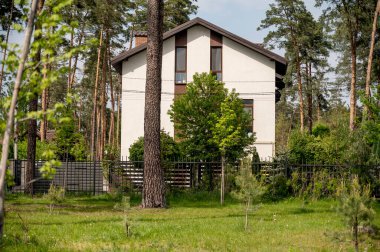 Ön cephesi ve iki katlı kahverengi çatısı olan yeni evin güzel dış görünüşü. Köyde çam ormanlarıyla çevrili beyaz evler. Evin etrafında çeşitli ağaçlar var.. 