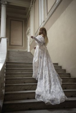 Peri prenses gibi uzun açık renk fantezi balo elbisesi giymiş güzel sarışın. Taş sarayda balkonlu bir kalede yürüyor. Merdivenlerde dikilip romantik şatonun merdivenlerini çıkıyorum.