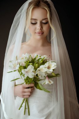 Camın yanında beyaz bir elbise ve bir buket zambak olan sarışın bir gelinin portresi. Minimalist iç mekan, karanlık arka plan, doğal aydınlatma. Makyajlı ve uzun saçlı gelin.