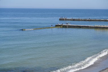 İki dalgalı deniz manzarası ve insanların balık tuttuğu bir rıhtım. Mavi deniz ve gökyüzü mavisi arka plan. Sabah manzarası sakin yaz, berrak gökyüzü. Sakinleştirici panorama meditasyona ilham verir..