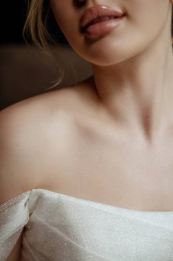 Makyajlı, pürüzsüz tenli, pembe dudaklı, gelinlikli güzel bir gelin. Genç bir kızın yakın plan portresi. beyaz elbiseli dudaklar ve omuzlar.