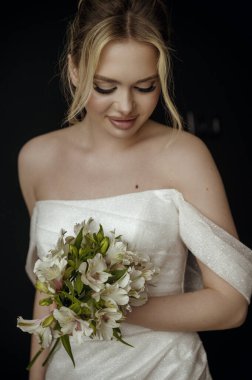 Elinde zambak buketi olan genç sarışın gelin. Kız gülümser, yere bakar. Omuzları açık şık bir elbise. Elinde çiçek tutan bir kadın. Yüksek kalite fotoğraf