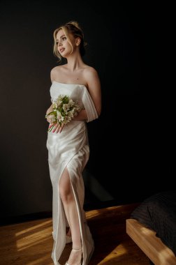 Elinde zambak buketi olan genç sarışın gelin. Kız gülümser, yere bakar. Omuzları açık şık bir elbise. Elinde çiçek tutan bir kadın. Güzel bir düğün buketi tutan şık bir gelin.