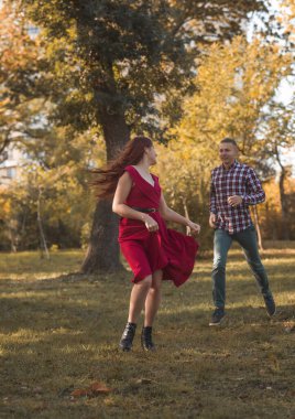 Genç aşık çift sonbahar parkında dinleniyor. Kaçıyorlar, eğleniyorlar ve gülüyorlar. Kırmızı elbiseli kız, altın sonbahar arka planına karşı. Romantizm kavramı, aşık olmak.. 