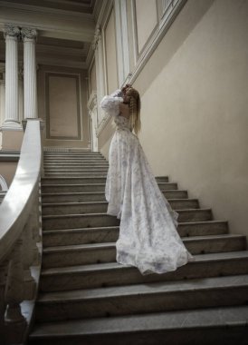 Sarı saçlı, uzun açık renkli fantezi balo elbisesi giyen peri prenses gibi. Soluk mavi çiçekli beyaz elbise. Taş sarayda balkonları ve merdivenleri olan bir şatoda yürüyor., .