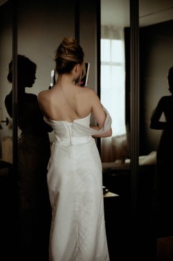 Gelin, aynaya bakar ve telefonda kendi fotoğrafını çeker. Selfie çekiyor. Uzun ve zarif bir elbisenin korsesinin arkasından manzara.