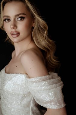 Genç bir portre, dalgalı saçlı sarışın bir kadın. Uzun saç stili olan güzel bir model. Mükemmel makyajlı ve şekilli bir sarışın. Omuzları açık beyaz bir elbise içinde..