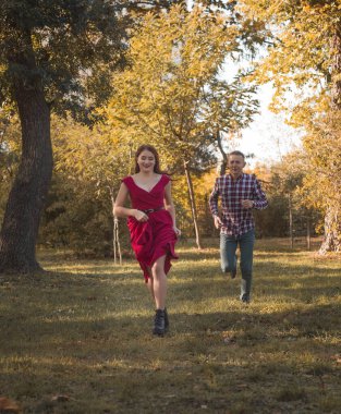 Genç aşık çift sonbahar parkında dinleniyor. Kaçıyorlar, eğleniyorlar ve gülüyorlar. Kırmızı elbiseli bir kız, altın sonbahar geçmişine karşı kareli tişörtlü bir adam. romantizm kavramı