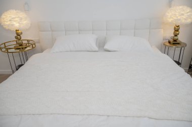 Tertemiz beyaz yatağı olan, rahat, modern bir otel odası. Oda minimalist tarzda beyaz tüy başucu lambalarıyla süslenmiş. Yumuşak ışıklandırma rahat bir atmosfer yaratır.