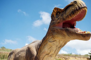 Dinazor Yapay, Tyrannosaurus 'un devasa heykeli, gökyüzü ve kayaların arka planına karşı. Kopyalamak için yer var. Ağzı açık bir dinozor.. 