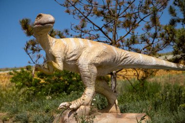 Uzun kuyruklu dinozor heykeli. Parktaki ağaçlar arasında dinozor figürü. Mavi gökyüzü ve ağaçların arka planına karşı. kopyalama alanı. yatay resim