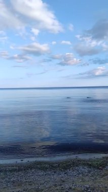 Sakin deniz yüzeyi bulutları yansıtıyor. Koyu mavi gökyüzü. Denizde kayalar ve büyük kayalar.