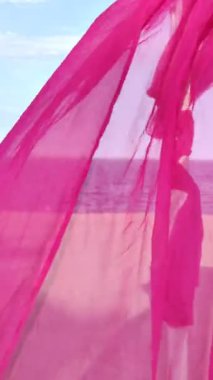 Pembe perde, kumlu bir kumsalın ve denizin arka planında dalgalanıyor. Pembe bir perdenin ardındaki deniz manzarası rüzgarda dalgalanıyor. Yaz tatili konsepti, plaj eğlence alanları. Rahatlamak için çardak