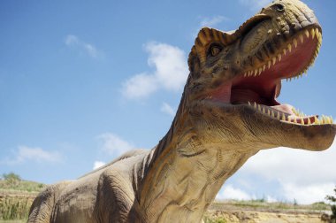 Dinazor Yapay, Tyrannosaurus 'un devasa heykeli, gökyüzü ve kayaların arka planına karşı. Kopyalamak için yer var. Ağzı açık bir dinozor.. 