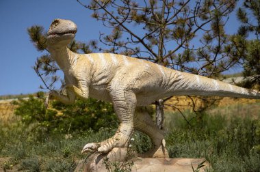 Odessa, Ukrayna - 30 Mayıs 2025: uzun kuyruklu bir dinozor heykeli. Parktaki ağaçlar arasında dinozor figürü. Mavi gökyüzü ve ağaçların arka planına karşı. kopyalama alanı. yatay resim