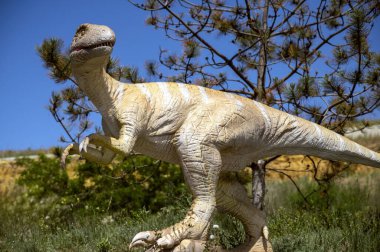 Uzun kuyruklu dinozor heykeli. Parktaki ağaçlar arasında açık sarı dinozor figürü. Mavi gökyüzü ve ağaçların arka planına karşı. kopyalama alanı. yatay resim