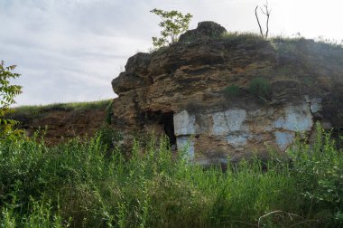Kayalıklarda terk edilmiş mağara evi. Mağara eski şehir. Mağaralara giriyoruz. Güneşin puslu ortamında nefes kesici bir manzara. Kayanın etrafındaki yemyeşil. Avrupa 'daki yeraltı mezarlıkları. taş üretim ve taş ocağı