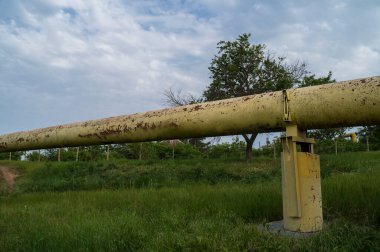 Gaz borusu tarladan geçiyor. Çapı sarı olan dev boru kırsal arazinin arka planında yeşil çimenler var. Ekolojik güvenlik ve altyapı kavramı.