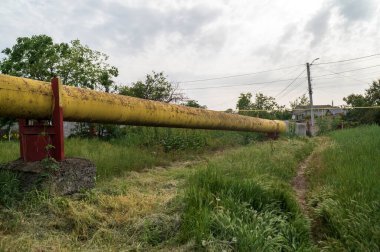 Gaz borusu tarladan geçiyor. Kırsal arazinin arka planına karşı çapı sarı olan dev bir boru. Ekolojik güvenlik ve altyapı kavramı.