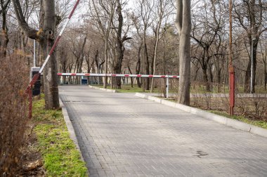 Otomatik bariyer, yeşil park alanının girişindeki güvenlik sistemi. Yol kenarında ağaçlar olan bir patika. Yüksek kalite fotoğraf