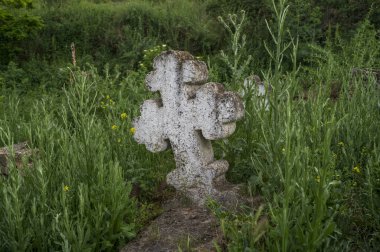 Eski bir mezarlıkta Hristiyan haçı oyulmuş antik bir taş. Haçın ucunda yuvarlak bir şekil var. Taş oymacılığı. Huzurlu bir kilise bahçesindeki mezar taşlarının görüntüsü.