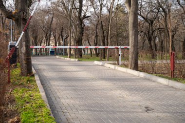 Otomatik bariyer, yeşil park alanının girişindeki güvenlik sistemi. Yol kenarında ağaçlar olan bir patika.