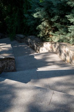 Doğayla çevrili gölgeli taş merdivenler aşağı iniyor. Şehir parkında taş basamaklı merdivenler.