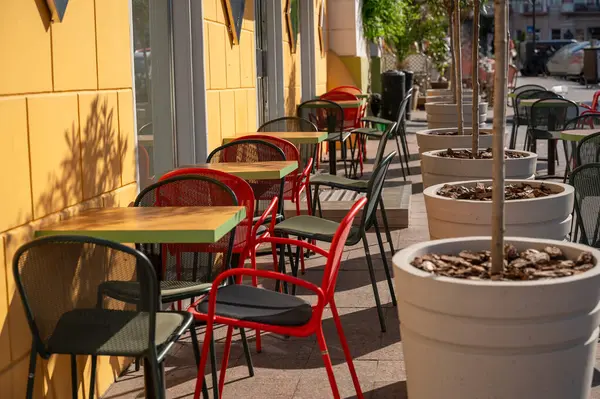 Parlak kırmızı, sarı ve yeşil mobilyaları ve büyük kaplarda bitkileri olan sokak kafeleri. Avrupa 'da aydınlık bir yaz gününde, sokakta boş bir kafe. Turizm ve seyahat kavramı