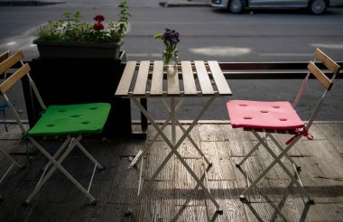 Sabahları, güneş ışığında, sokak kafeteryasında. Boş teras, parlak sandalyeler ve masanın üzerinde cam şişeler içinde yabani çiçekler. Bir Avrupa şehrinde masalı teras ziyaretçileri bekliyor