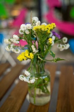 Kırsal buket yabani çiçekleri cam şişede, ahşap masa üzerinde su ile, açık havada doğal bahçe ortamında. Yaz kırsal atmosferi, taze ve basit çiçekli durgun hayat