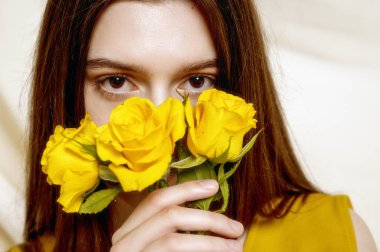 Esmer, koyu renk gözlü, elinde bir buket sarı gülle, yüzüne yakın bir yerde. Kız kameraya bakıyor. Cilt bakım ürünleri, kozmetik ürünleri, spa, krem.