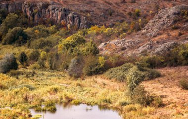 Dağ kanyonunda harika bir sonbahar. Kocaman granit kayalar. Ukrayna 'daki Aktovsky Kanyonu' nda kayalıkları, ormanları ve çayırları olan bir dağ gölü var. Sarı ve kırmızı ağaçlar ve gölün etrafındaki çayırlar
