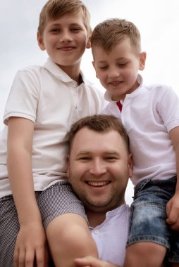 Babamın iki oğlunu sahilde omuzlarında taşırken. Baba ve çocuklar gün içinde kumsalda eğleniyorlar. Baba ve oğulları sahilde birlikte yürüyorlar. Birbirine bağlı aile kavramı.