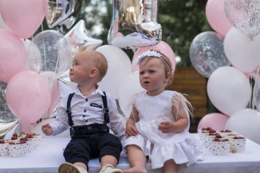 Erkekler ve bir kız ilk doğum günlerini kutlarlar. Giyinip kuşanmış, balonların arka planında yan yana oturuyor. Çocuklar dışarıda parti veriyor. Küçük prenses ilk doğum gününde.