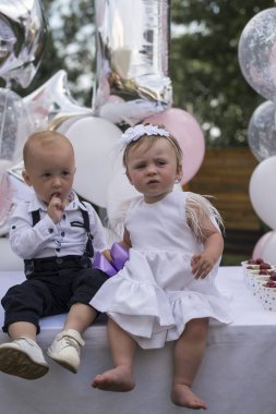 Erkek ve kız, ikizler ilk doğum günlerini kutlarlar. Balonların arka planına karşı giyinmiş, yan yana oturuyorlar. Çocuklar dışarıda parti veriyor. İlk doğum gününde tatlı küçük prenses..