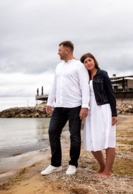 Mutlu çift el ele tutuşup, yumuşak kum ve nazik dalgalarla çevrili güzel bir sahilde birbirlerine bakıyorlar. Heyecanlı, güzel genç çift, aile babası, beyaz elbiseli kadın ve erkek.