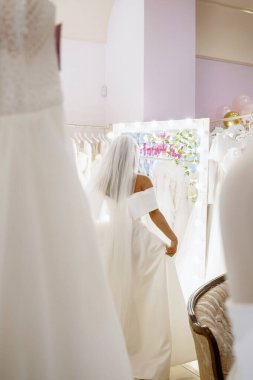 Muhteşem gelinlik ve duvak giymiş bir gelin aynanın önünde dikilip gelinlik mağazasında elbise deniyor. Gelin büyük bir ayna önünde gelinlik seçiyor, genel plan bu.