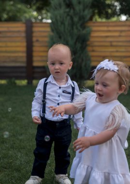 Giyinip süslenmiş şirin çocuklar sabun köpükleri tarafından mutlu ve şaşırtılıyor. Parktaki kız ve erkek sokakta bir sabun köpüğü gösterisine katılıyor.