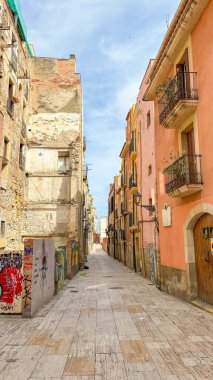 Canlı bir şehirde, renkli binalar ve sokak sanatının yer aldığı dar bir cadde. Tarihi ve modern elementlerin karışımı dinamik bir şehir atmosferi yaratır. Tarragona, İspanya.