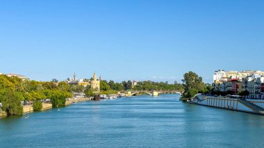 Seville 'in nehir kenarının manzarası, Guadalquivir Nehri' nin manzarası, tarihi simgeler, yemyeşil ve açık mavi gökyüzü altındaki renkli binalar..