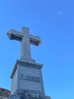 A granite cross memorial with a inscription, set against a clear blue sky and a crescent moon, capturing a peaceful and solemn moment in La Recoleta, Buenos Aires. clipart