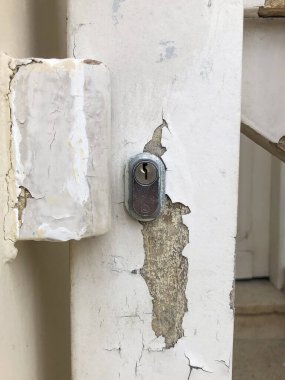 Close-up of a metal lock on a white wooden door with peeling paint, revealing textures and decay. Rustic and aged detail in an urban setting. clipart