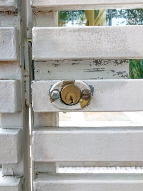 Close-up of a brass lock on a weathered white metal gate with peeling paint, capturing urban wear and rustic charm in a bright outdoor setting. clipart