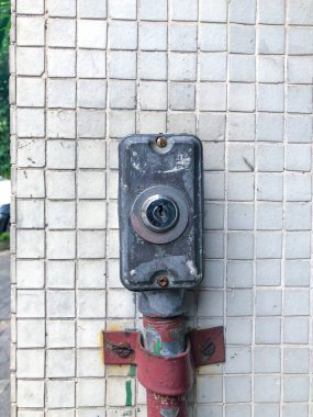 Metalik bir kilidin yakın plan resmi kırmızı bir boruyla döşenmiş döşemeli bir duvara monte edilmiş, şehir tasarımı ve endüstriyel detaylar açık hava ortamında sergileniyor..