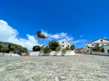 Göz kamaştırıcı bir günbatımı, yumuşak dalgaları ve kumlu kıyıları yansıtan canlı turuncu tonlarla gökyüzünü boyar. İki siluetli figür suyun kenarında yürüyor, arka planda dik duran görkemli bir uçurum var..