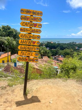 Göz kamaştırıcı bir günbatımı, yumuşak dalgaları ve kumlu kıyıları yansıtan canlı turuncu tonlarla gökyüzünü boyar. İki siluetli figür suyun kenarında yürüyor, arka planda dik duran görkemli bir uçurum var..
