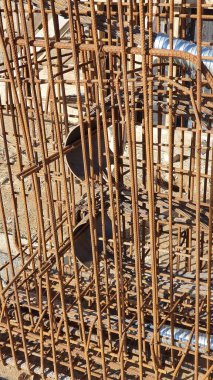 Metal inşaat yapılarından oluşan karmaşık bir ağı gösteren bir inşaat sahasının yakından görüntüsü. Paslı çelik çubuklar binanın sağlamlığı ve temeli için gerekli olan ızgara benzeri bir kalıp oluşturuyor..