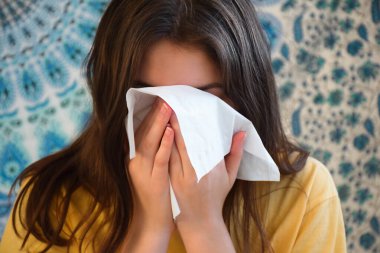 Genç kız burnunu silmek ya da hapşırmak için yüz kağıdı kullanıyor.